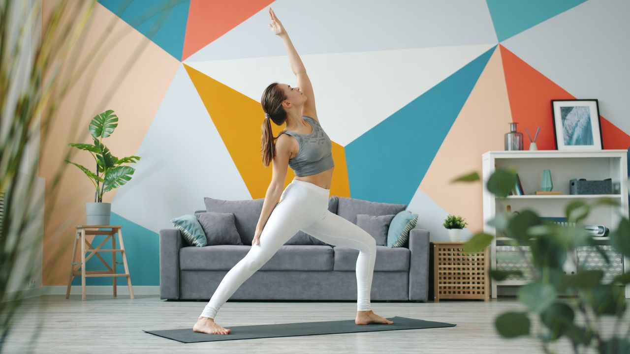 A young woman practicing yoga in a modern studio with a colorful geometric wall design.